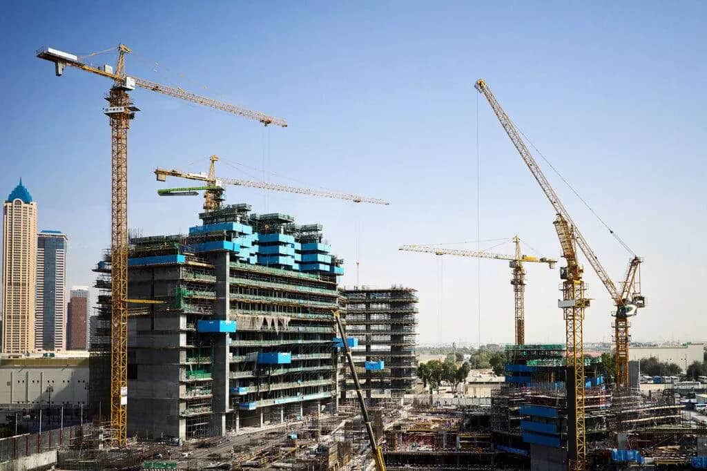 High-rise buildings under construction wrapped in scaffolding, with several tower cranes against a clear sky