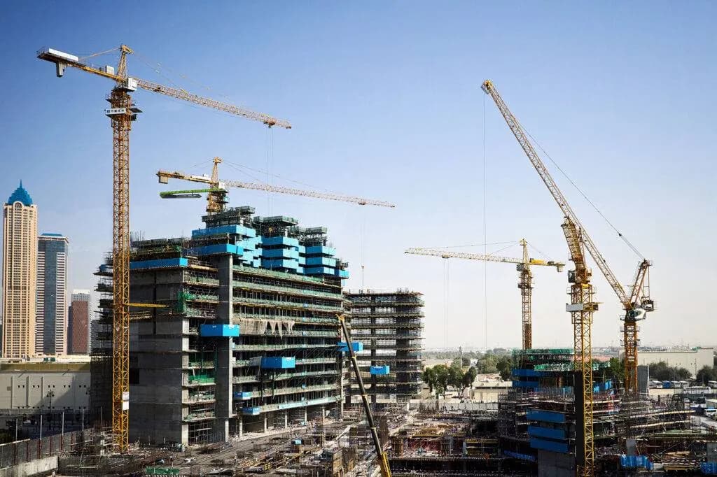 Tower cranes above high-rise buildings under construction, wrapped in scaffolding and safety screens on a busy site