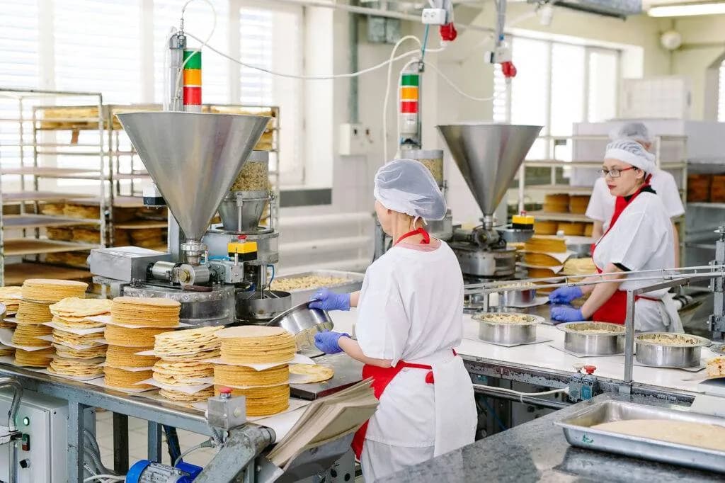 Food factory workers in hairnets, aprons and gloves handling pastry layers on a hygienic production line