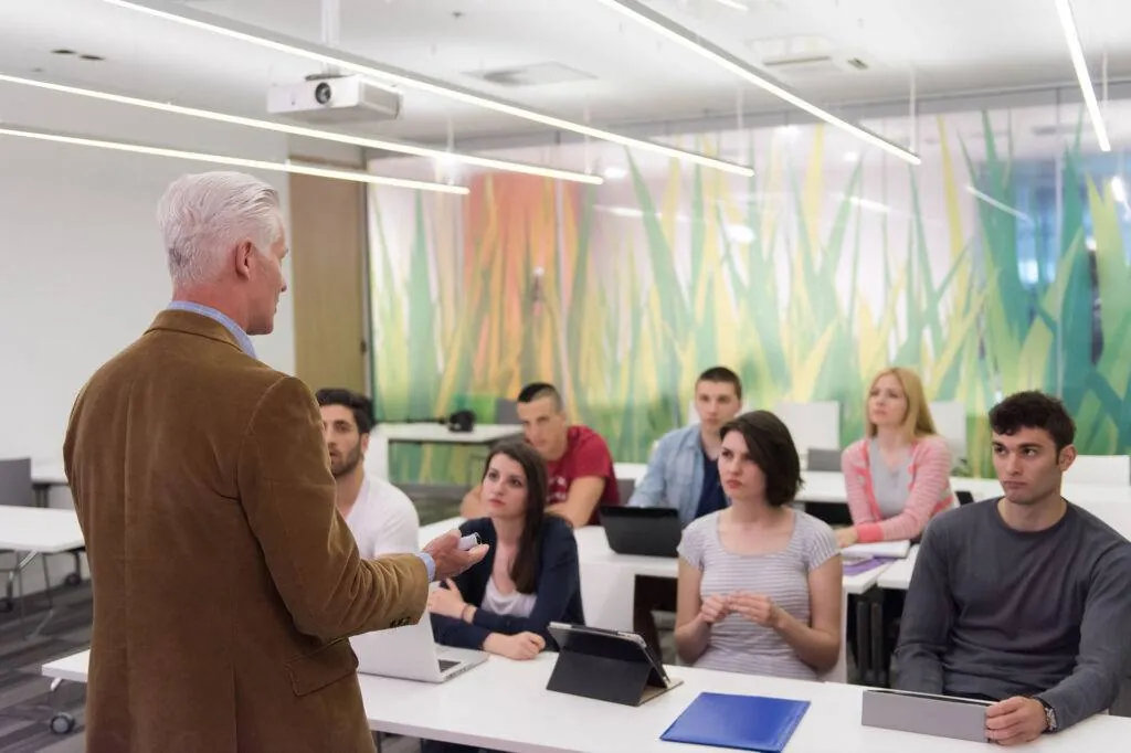 Presenter addressing seated delegates with laptops and tablets during a seminar in a modern classroom